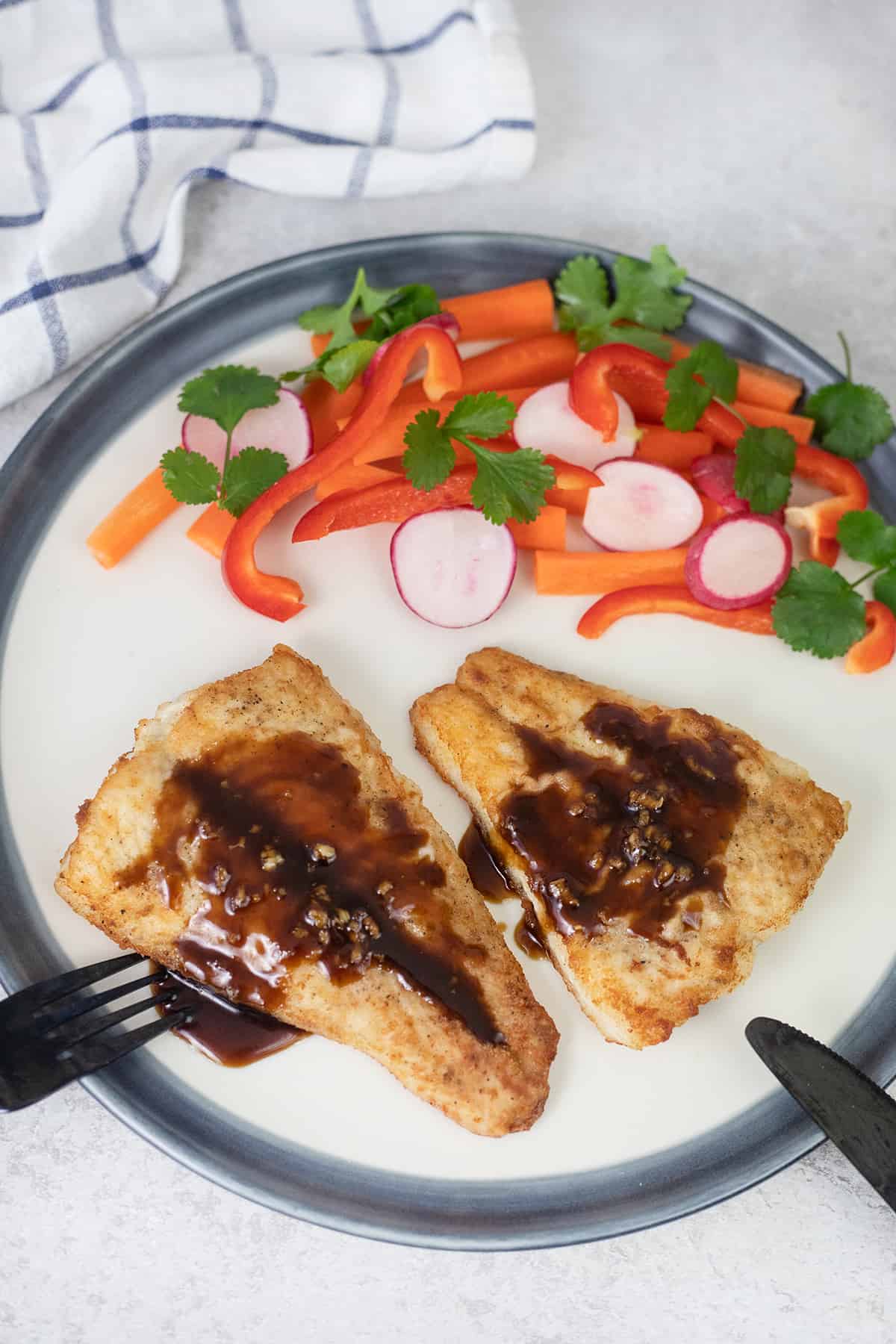 Two Sea Bass fillets in a plate with the Soy Sauce.