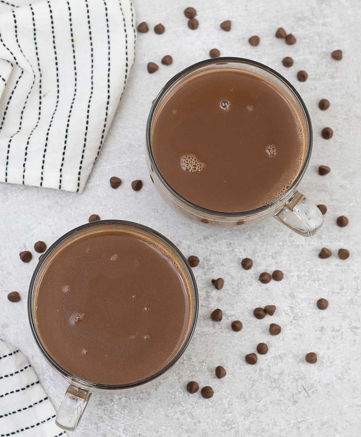 Chocolate Tea is in 2 large cups, and some chocolate chips are scattered.