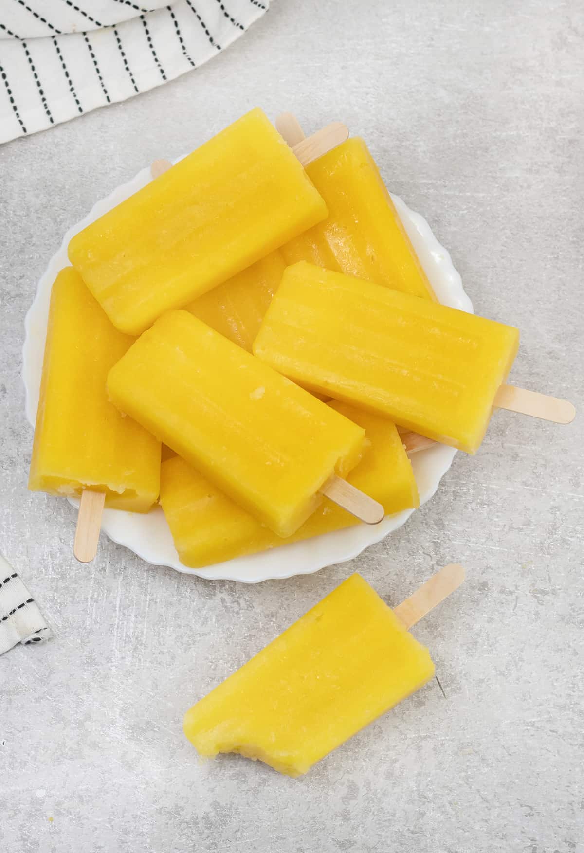 Mango popsicles in a serving plate and one of them is on the table.
