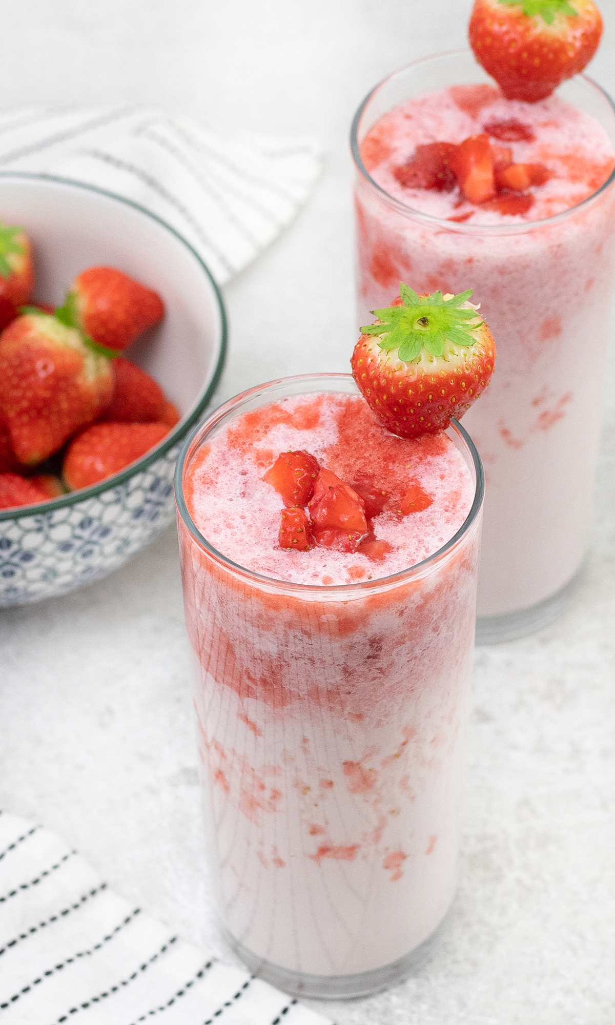 homemade Korean Strawberry Milk in glass and a big bowl of Strawberries is in the background.