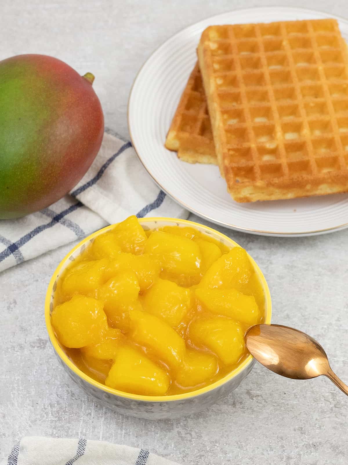 Mango Compote in a bowl, and waffles and mango in background.