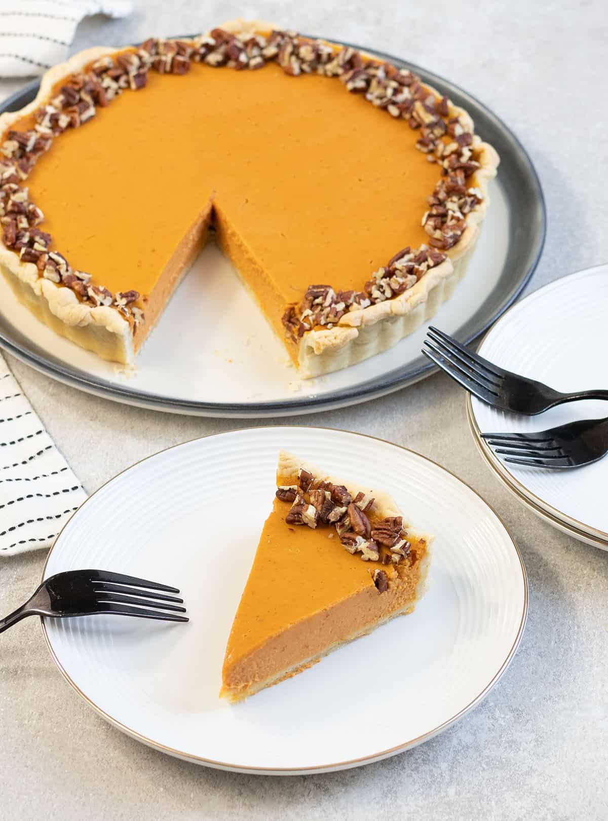 A slice of the pumpkin pie on a plate topped with pecans.