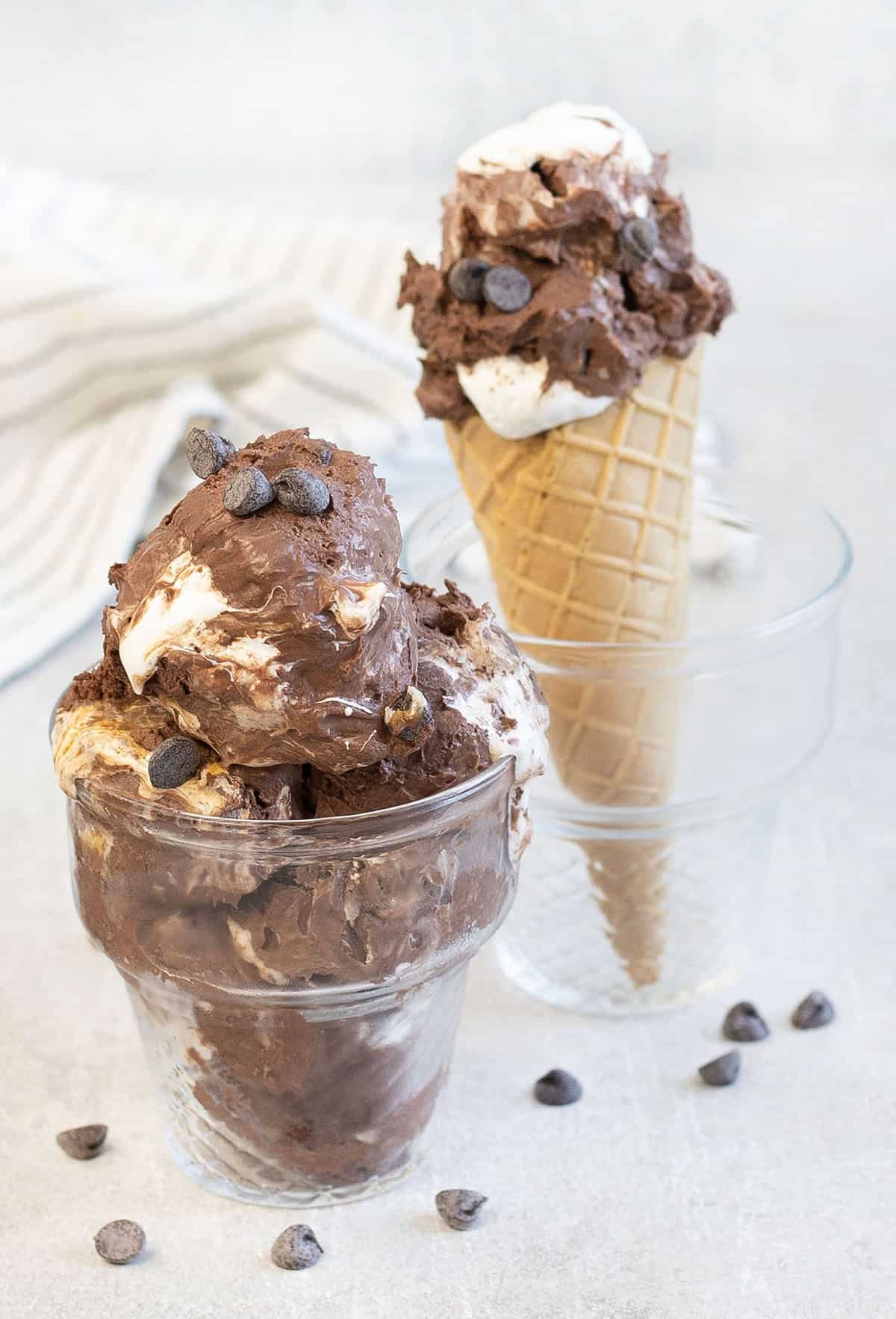 Chocolate marshmallow ice cream in a glass and a cone is in the background.