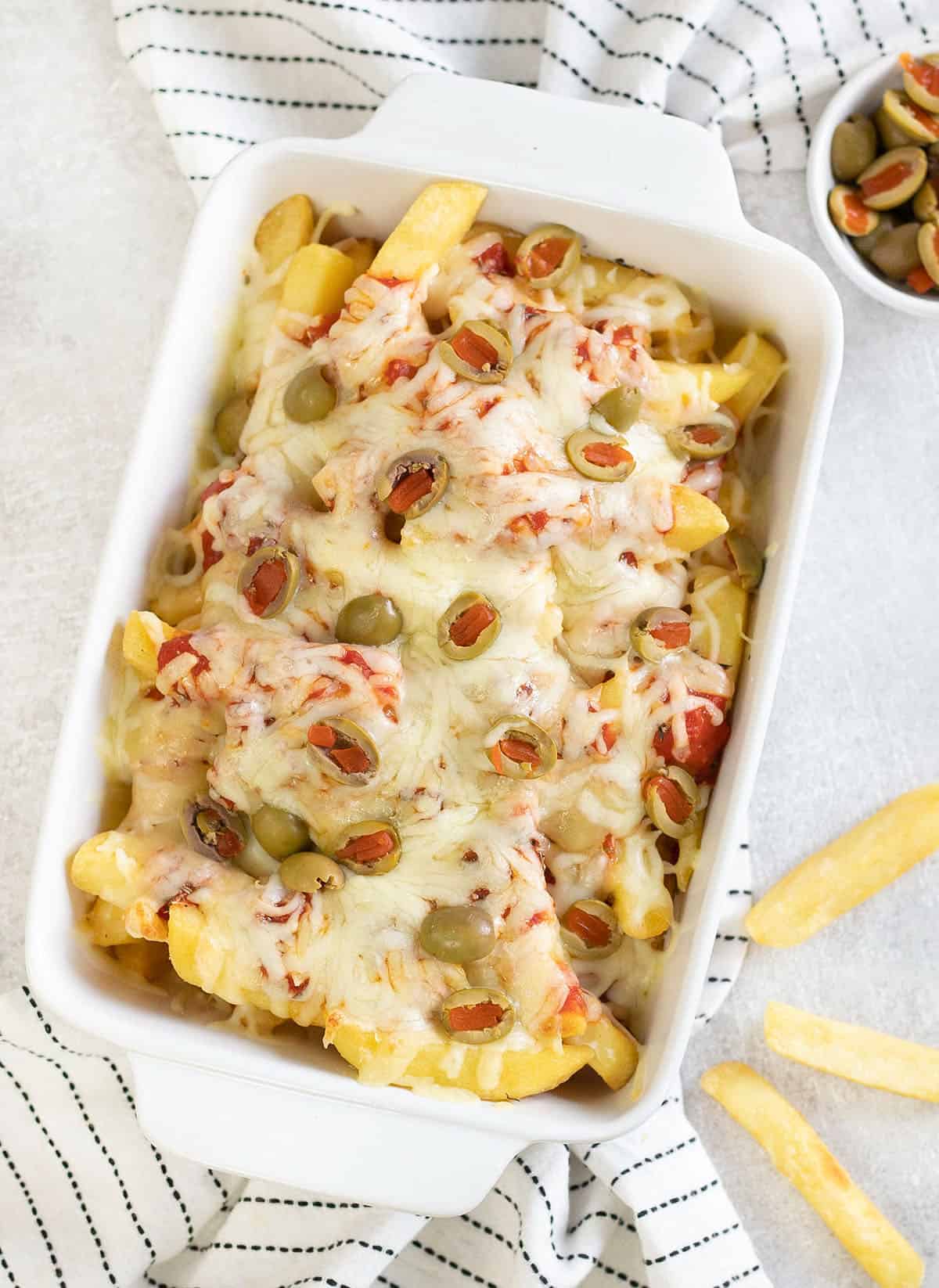 baking dish full of Pizza Fries topped with cheese and olives.