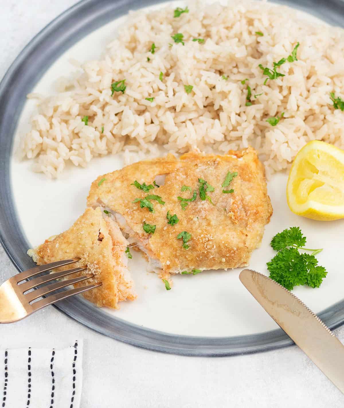 A crispy baked cod with parmesan and breadcrumbs crust cut with a fork.