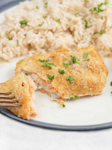 crispy baked cod with parmesan in a serving plate along with rice.