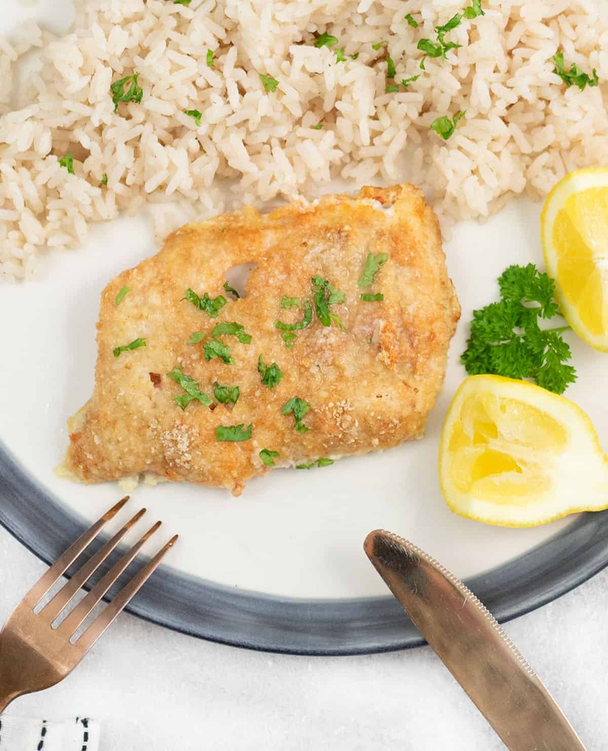 crispy baked cod with parmesan along with lemon wedge and white rice.