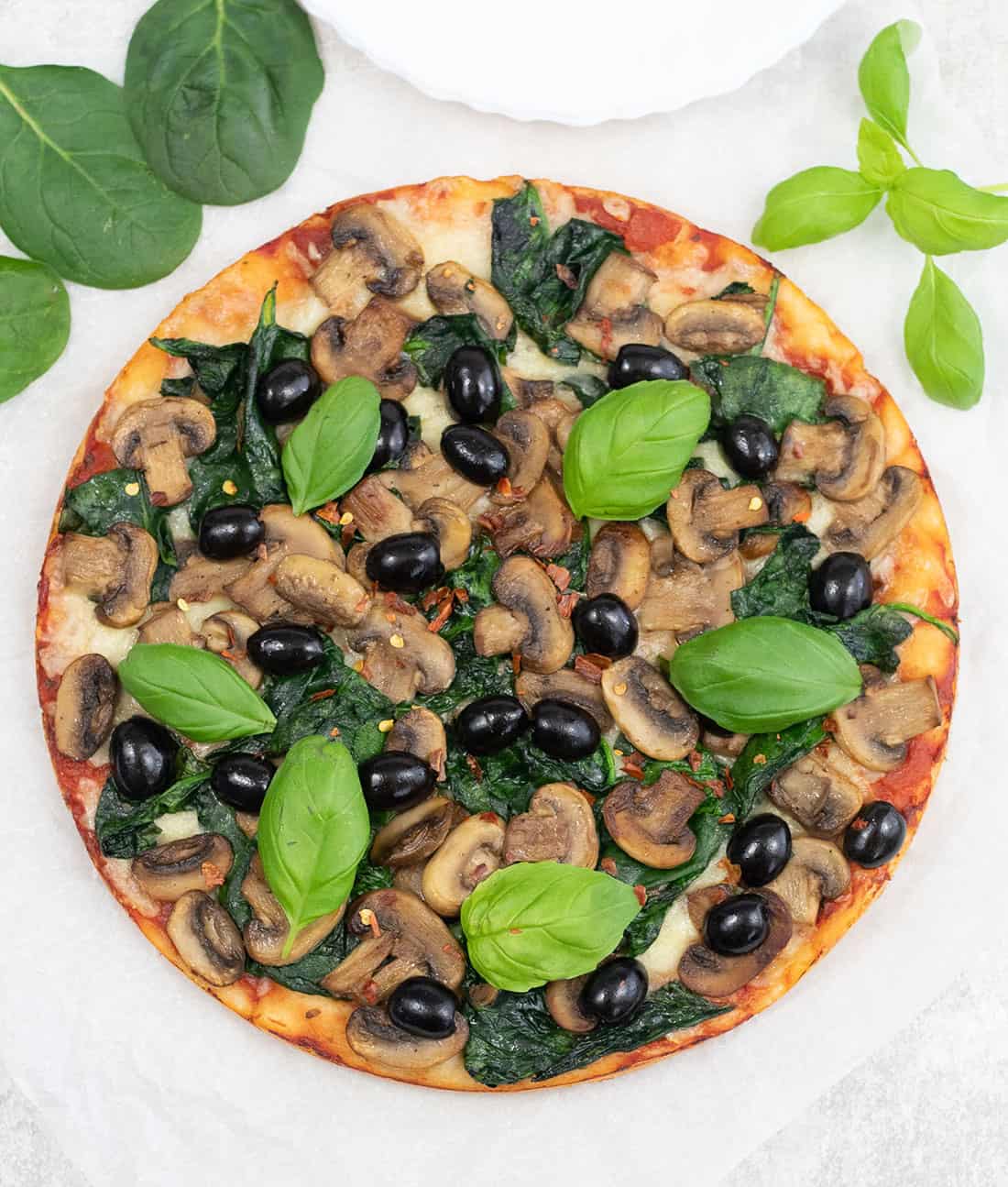 a whole fresh spinach mushroom pizza topped with basil leaves.