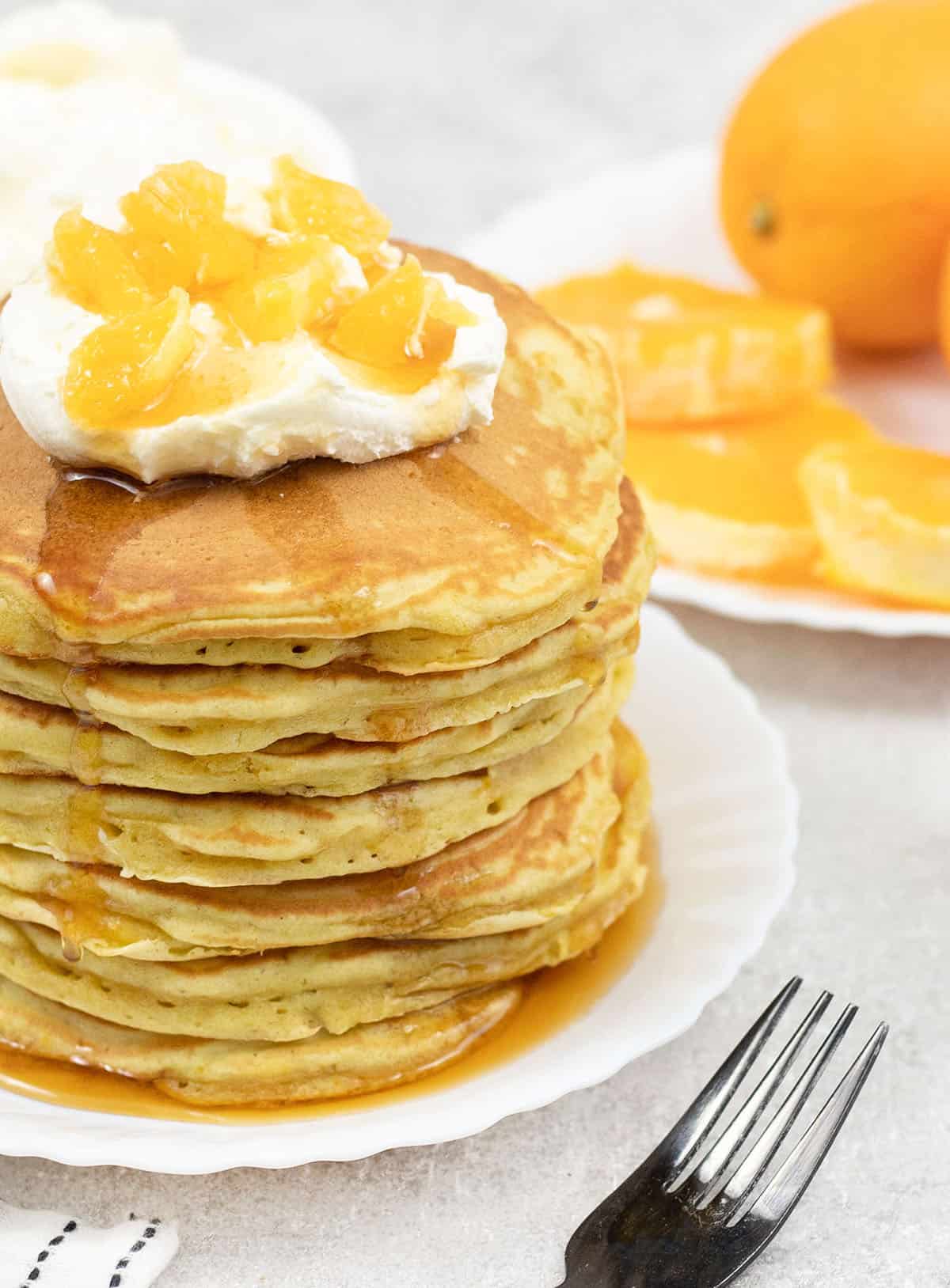 Orange Pancakes in a serving plate and some fresh oranges are in the background.