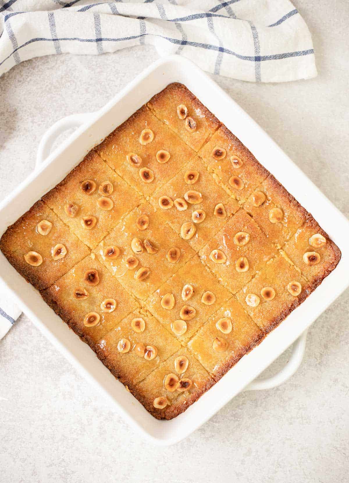 Egyptian Basbousa (Semolina Cake) fresh-out-of-the-oven in a white pan against a white surface.