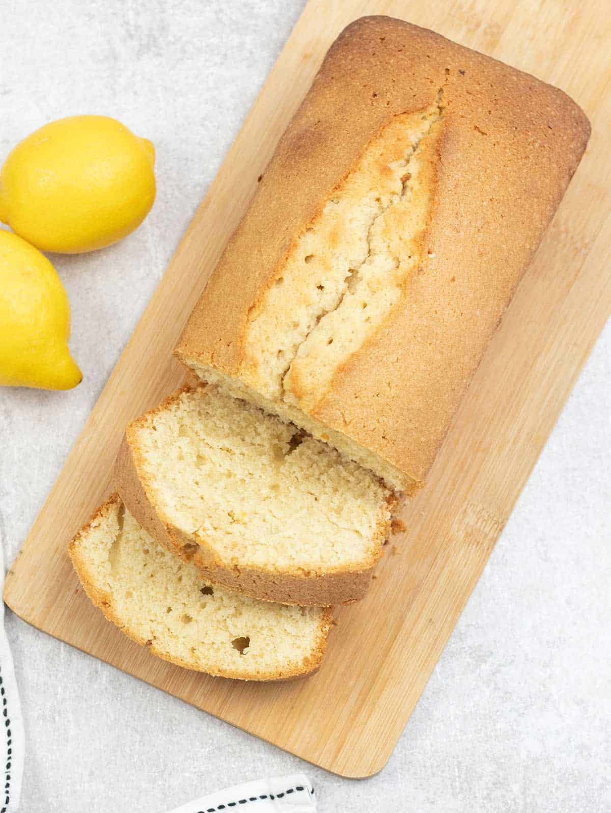 Whole loaf of Madeira cake is on a cutting board, and lemon is around.