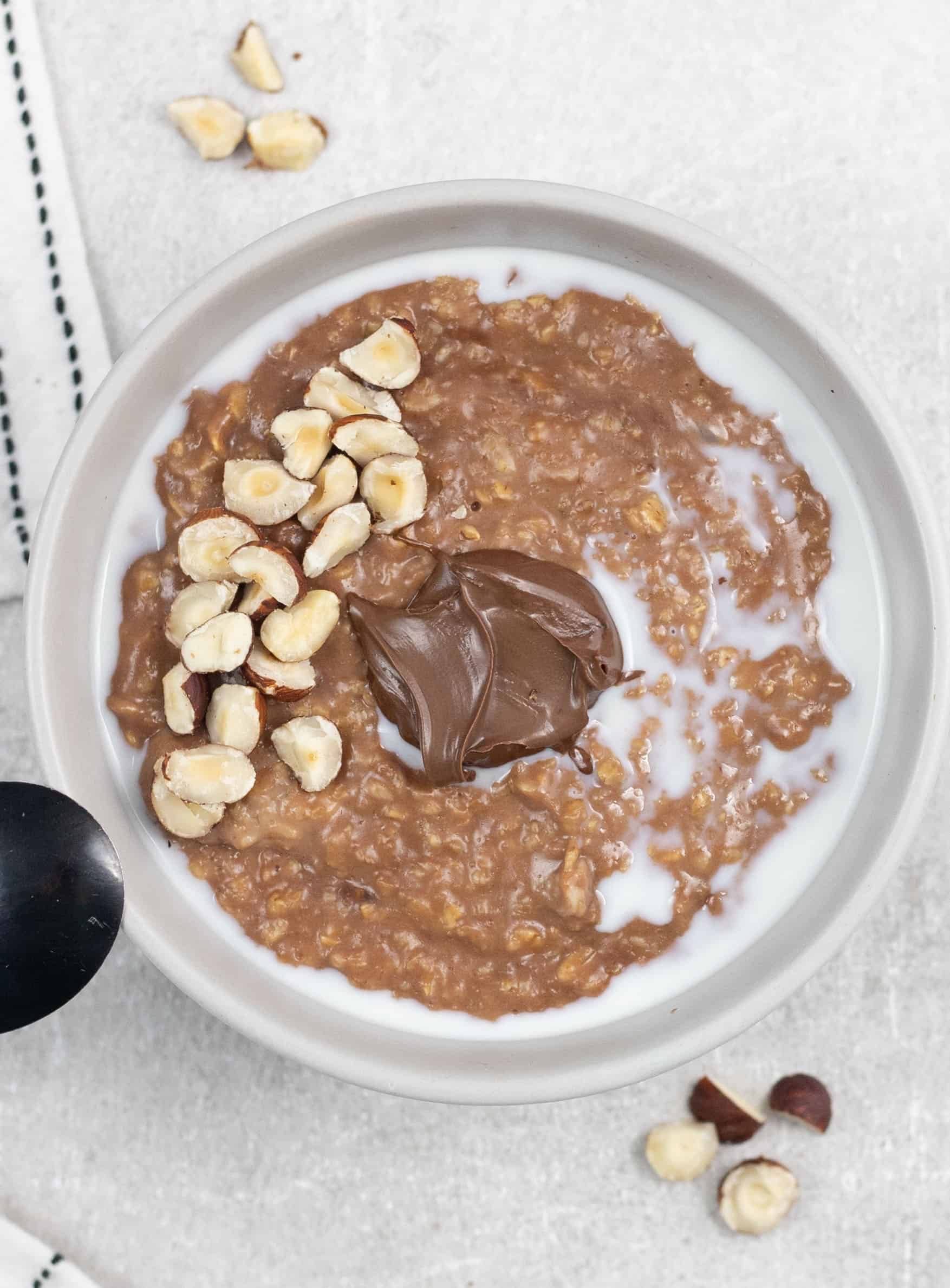 Nutella Porridge in a bowl topped with hazelnut and spoon of Nutella