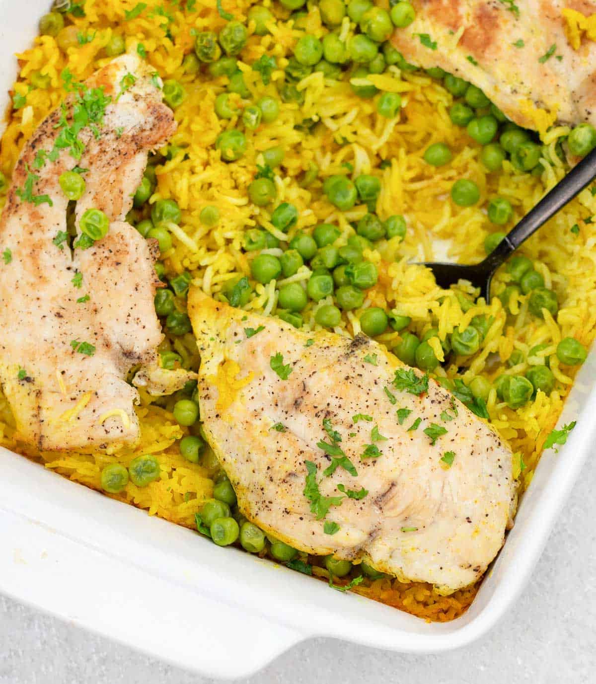 Scooping a chicken, peas and yellow rice from the casserole dish.