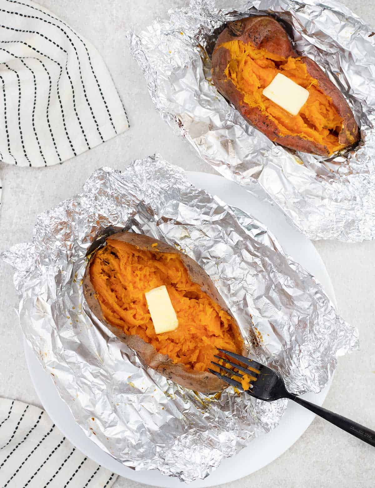 Baked Sweet Potatoes on top of Foil sheet  and the potatoes are topped with butter