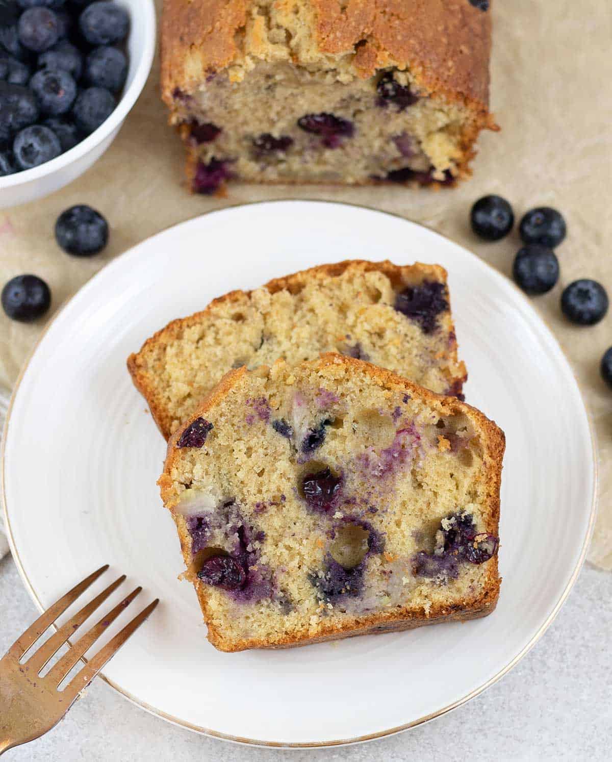 Blueberry Banana Bread slice in a plate and some blueberries in the background.