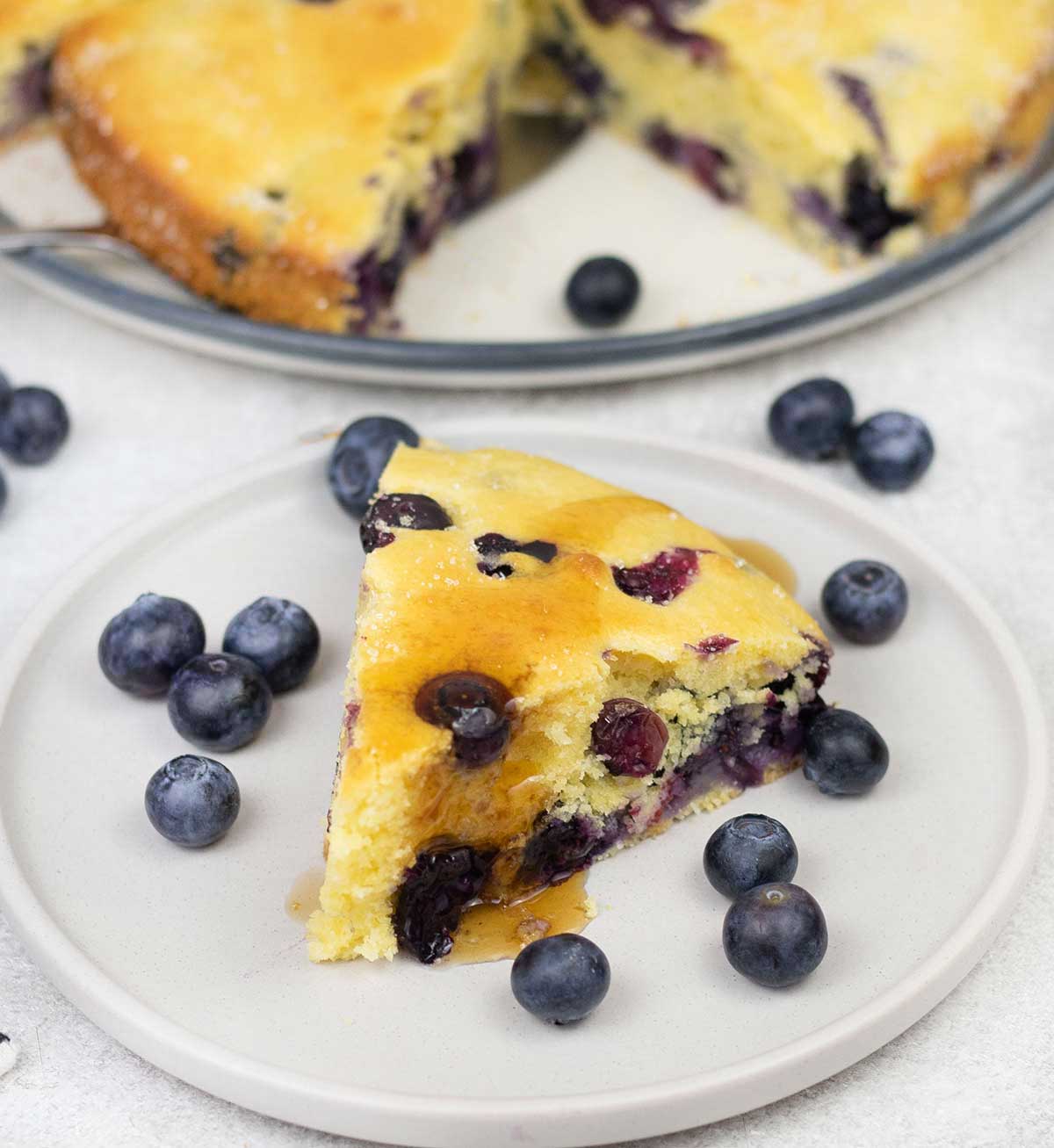 A slice of the blueberry cornbread and some blueberries are in the plate.