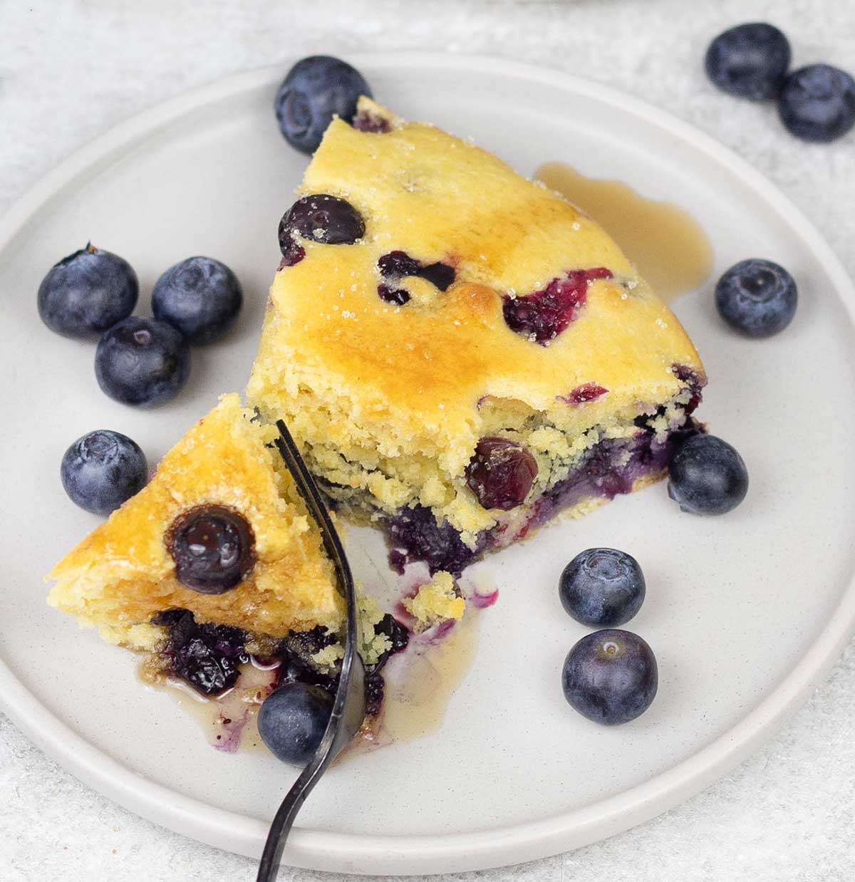 Close shot to a slice of the blueberry cornbread and some blueberries.