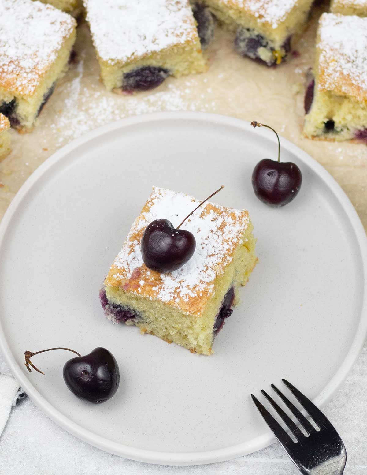 Piece of cherry cake on a plate along with some fresh cherries.