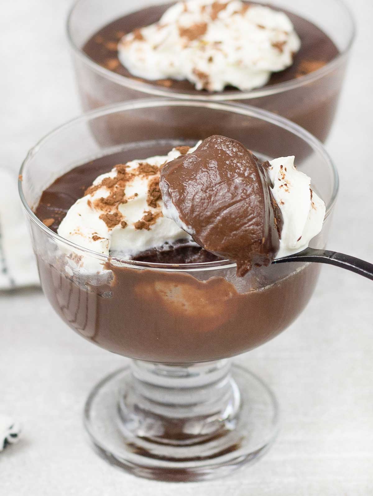 a spoonful of Chocolate Pots topped with whipped cream and cocoa powder.