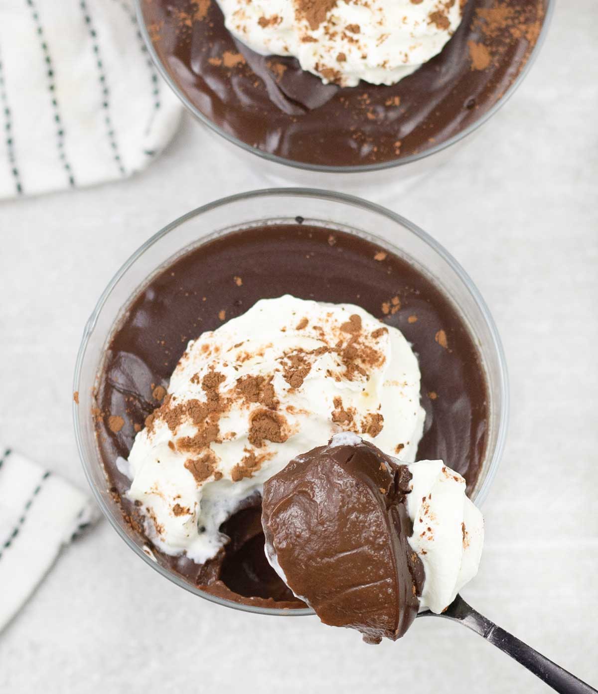spoonful of Chocolate Pots topped with whipped cream and cocoa powder.