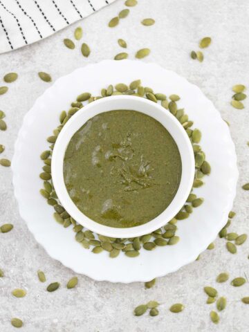 Pumpkin seed butter in a small bowl with pumpkin seeds around it.
