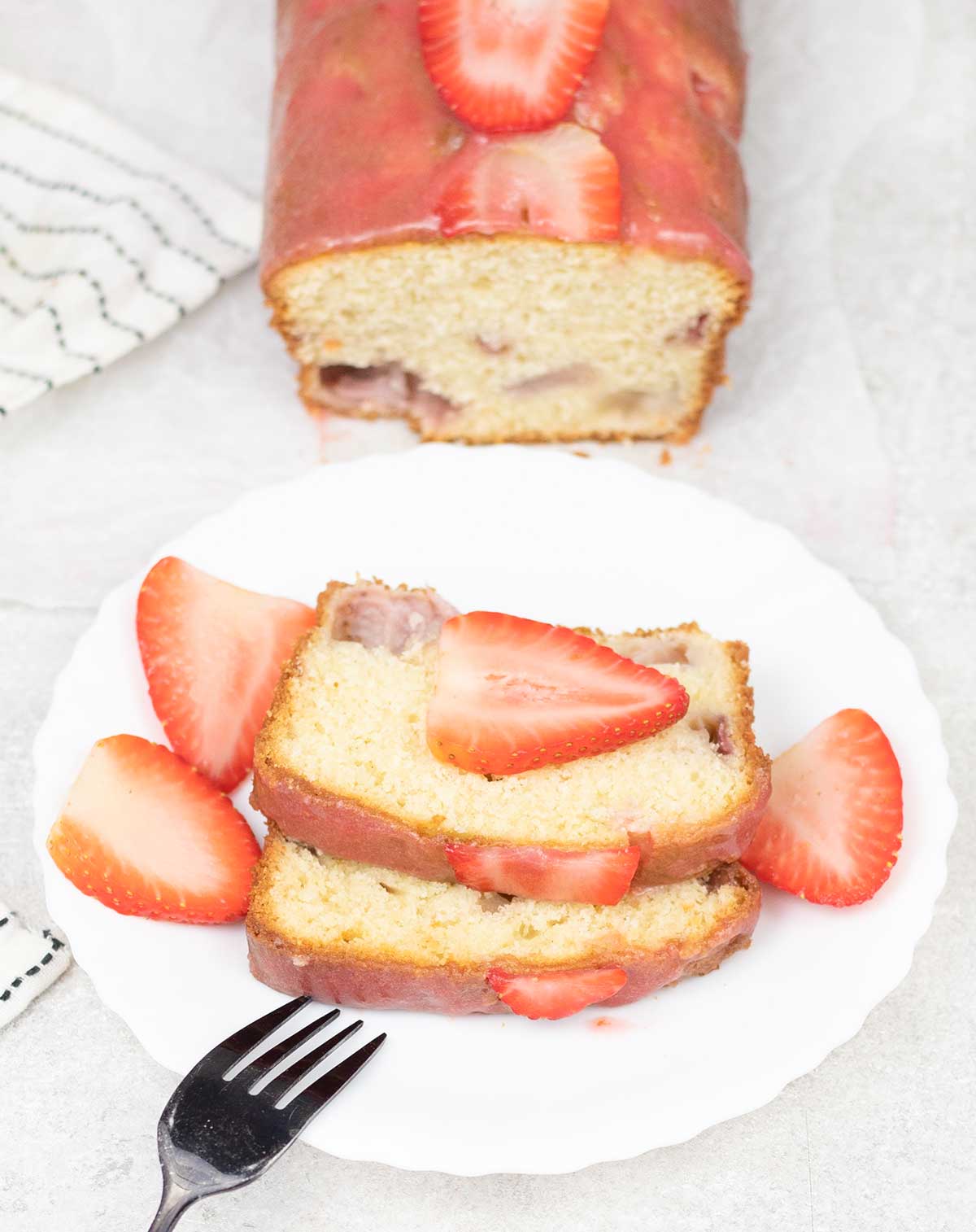 Slices of strawberry loaf cake topped with some fresh strawberries glaze.