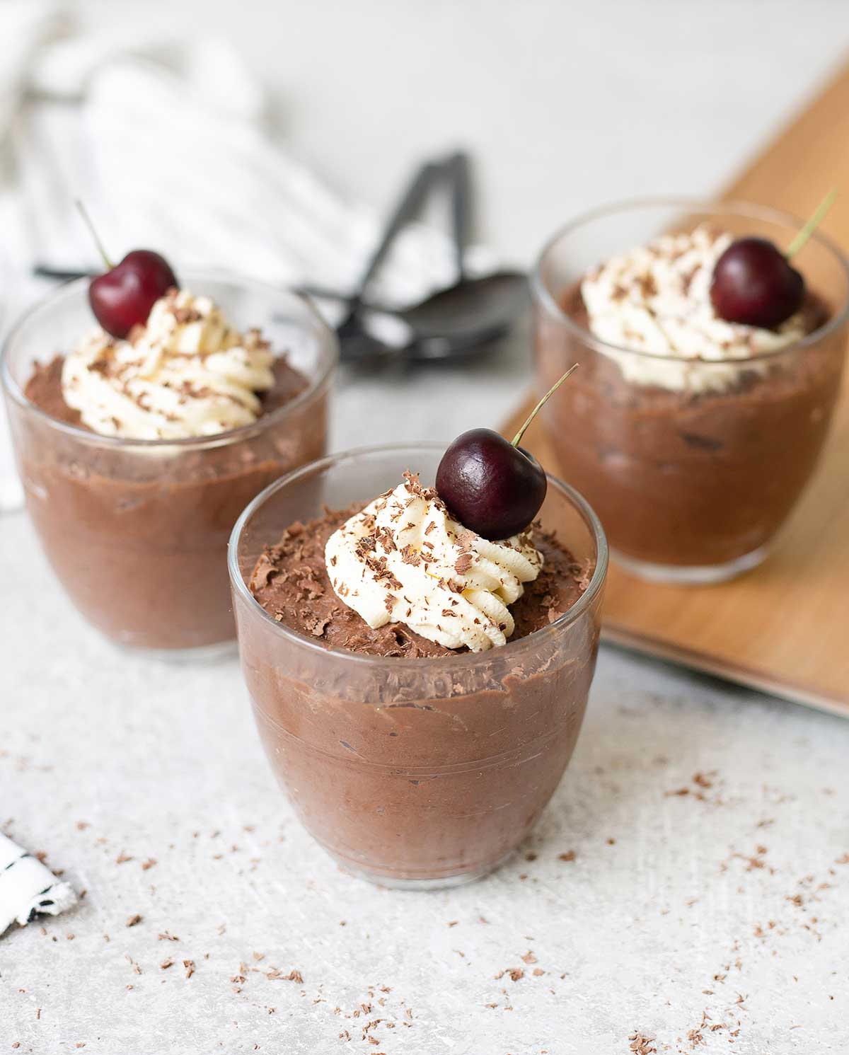 3 glasses of eggless chocolate mousse topped with fresh cherry.