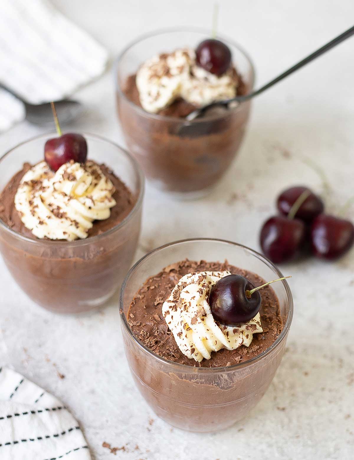 3 glasses of eggless chocolate mousse topped with fresh cherry and whipped cream.