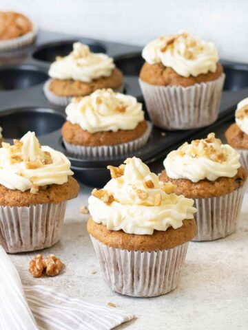 Carrot cake cupcakes topped with cream cheese frosting and walnuts.