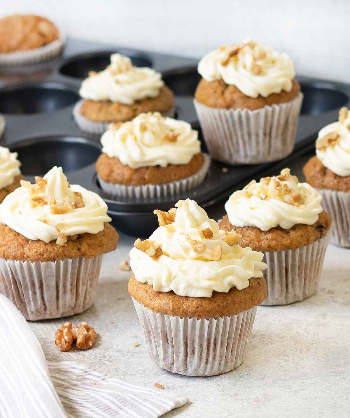 Carrot cake cupcakes topped with cream cheese frosting and walnuts.