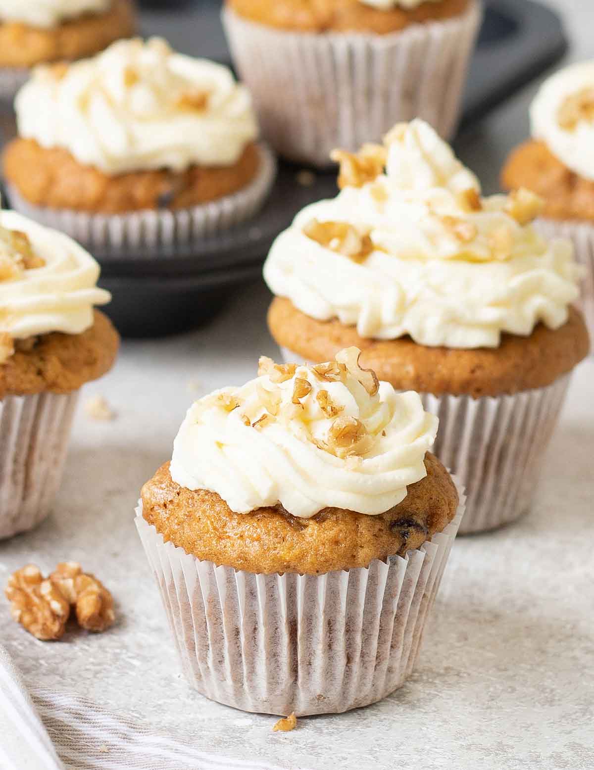 Carrot cake cupcakes and walnuts on a table.