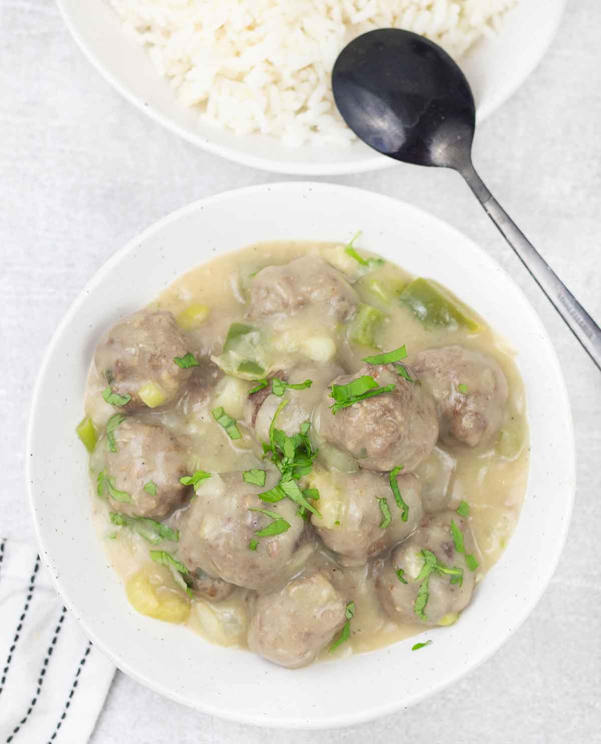 Cajun meatball stew in a bowl and a white rice bowl is in the background.