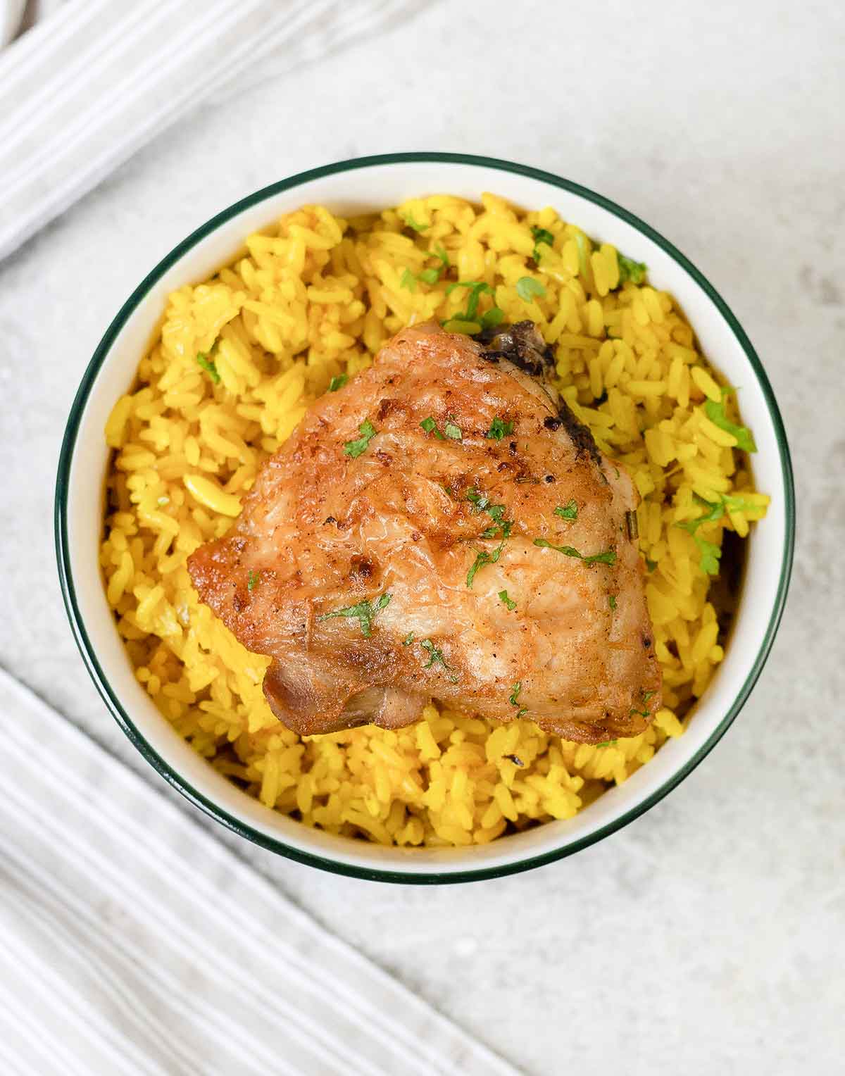 Bon in and skin on baked chicken thigh on top of yellow rice.