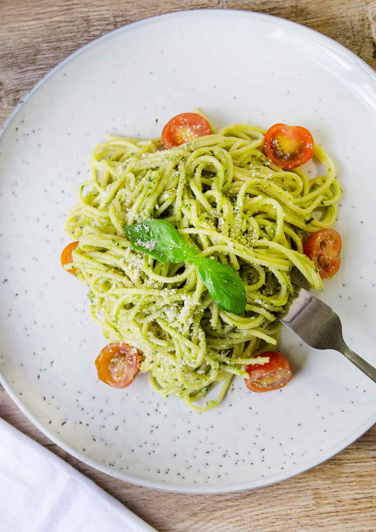 Creamy avocado sauce pasta in a plate along with some cherry tomatoes.