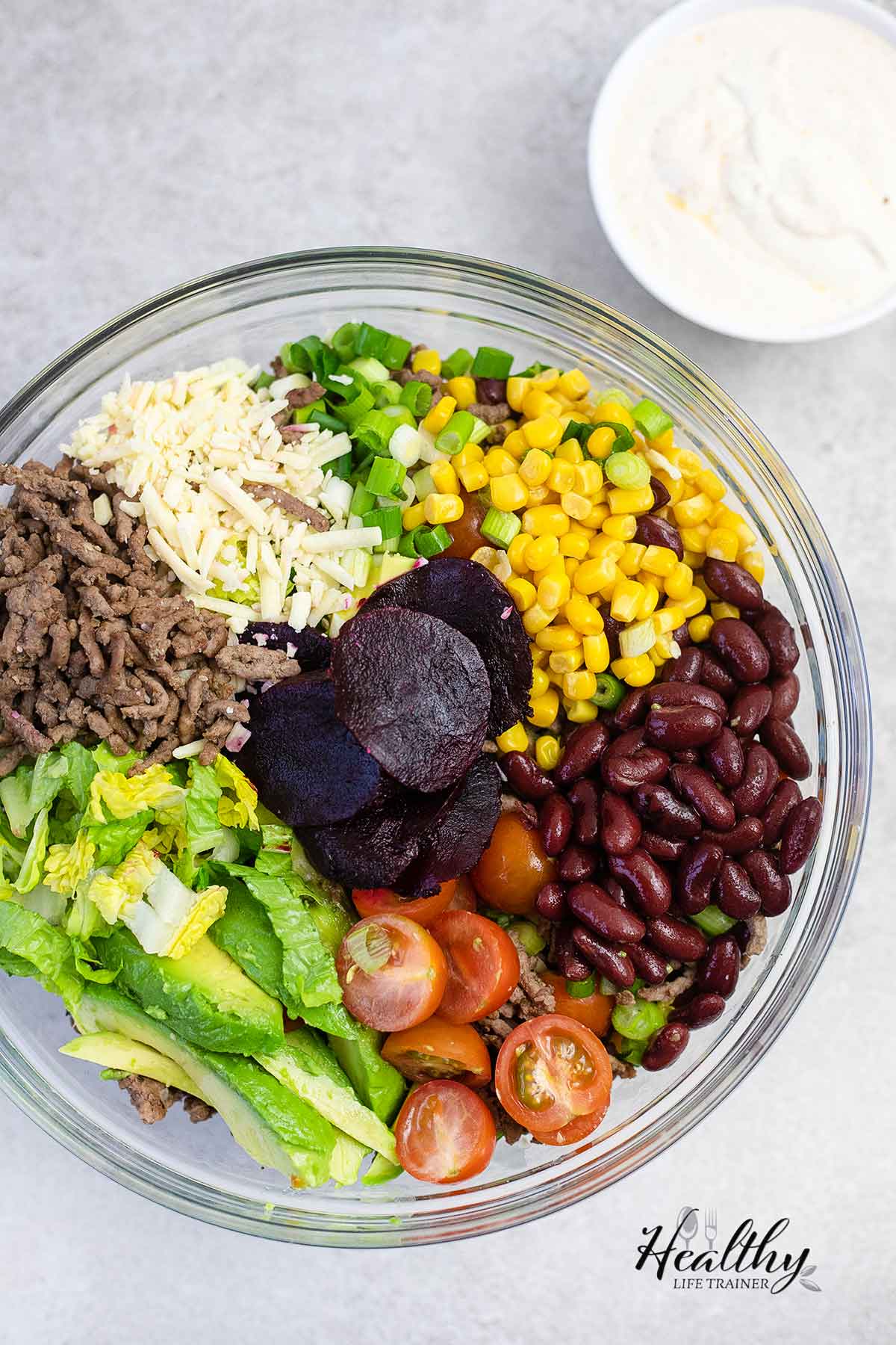 In a bowl, avocado, lettuce, tomatoes, green onions, beetroots, kidney beans, sweetcorn, cheddar cheese, and the cooked ground beef.