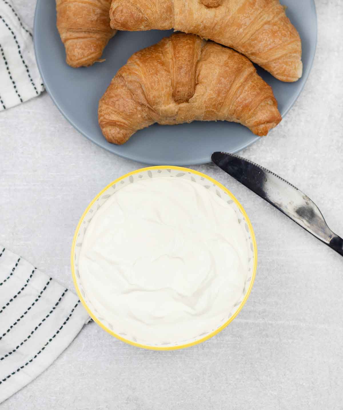 Homemade cream cheese in a bowl and croissant in a plate.