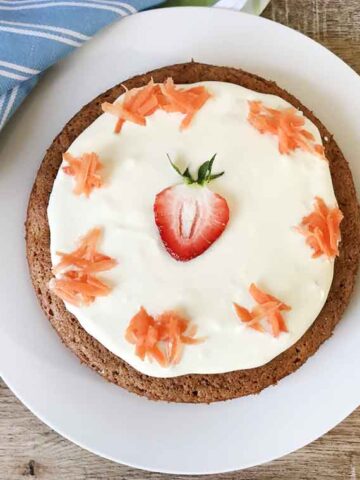 A whole gluten-free carrot cake made with almond flour and topped with shredded carrots.
