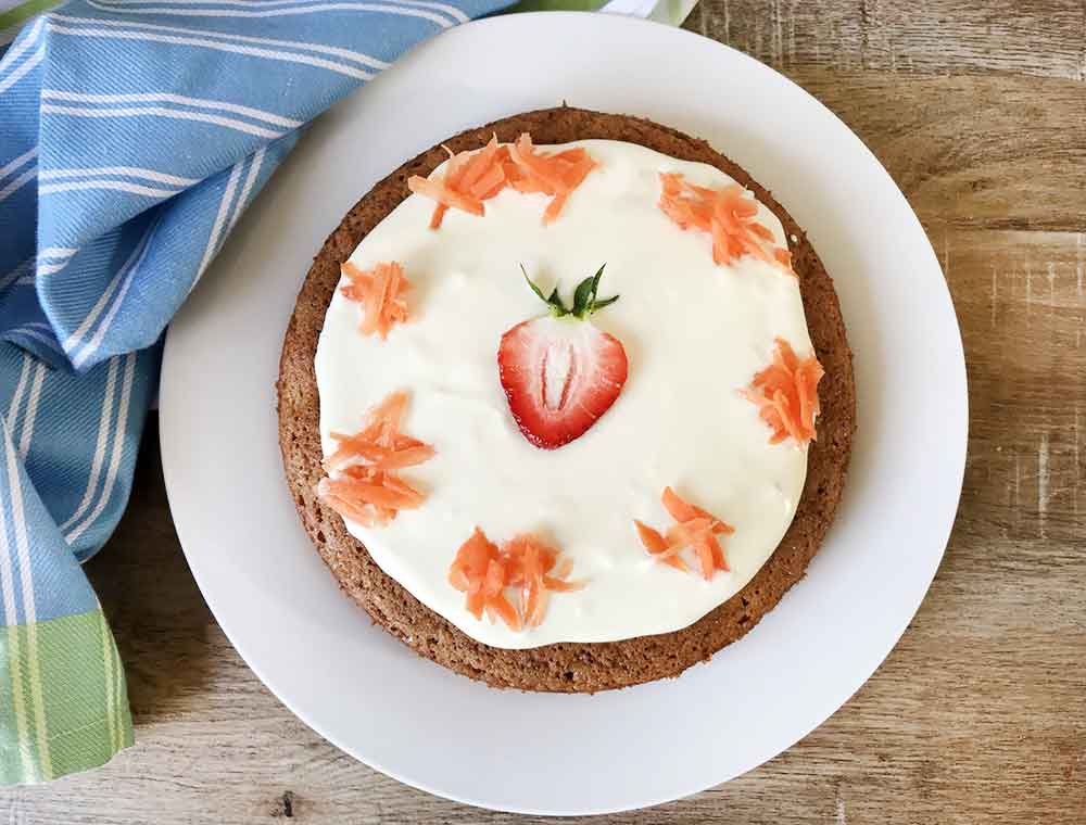 A whole gluten-free carrot cake made with almond flour and topped with shredded carrots.