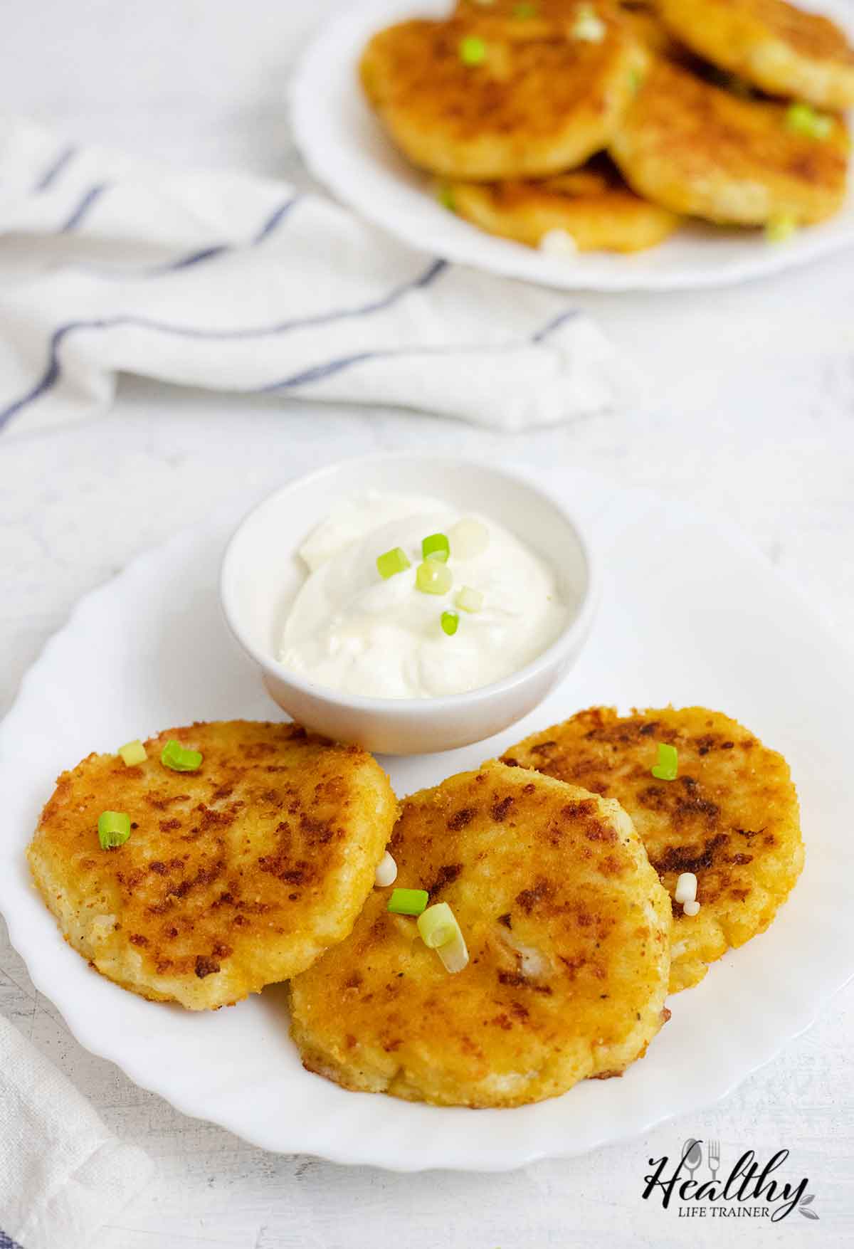 Leftover mashed potato pancakes on a plate and sour cream in a bowl.