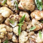 Vegan roasted cauliflower with garlic topped with fresh basil leaves.