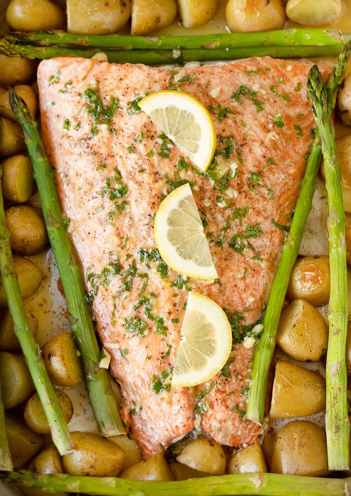 Salmon, asparagus and potatoes in a sheet pan topped with lemon slices.
