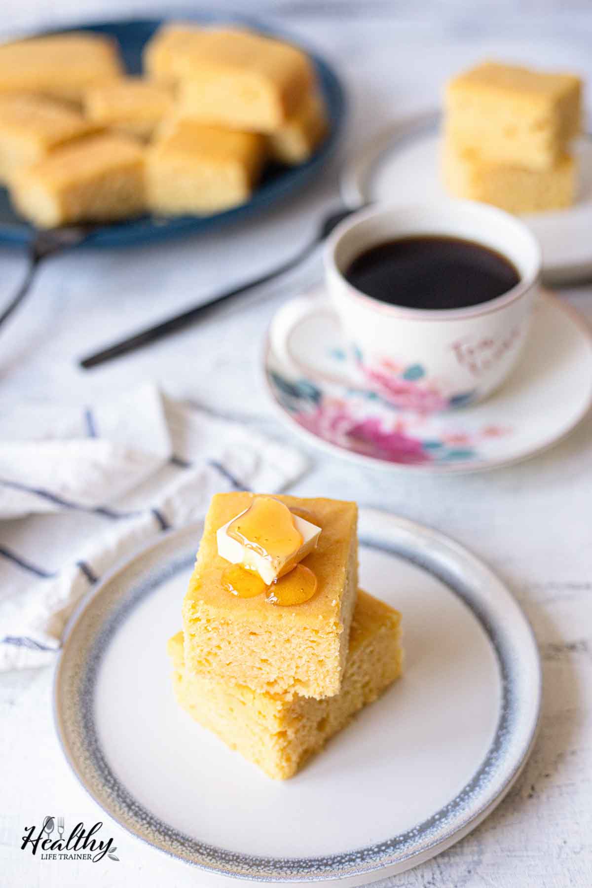 Cornbread cake is on a plate, and a cup of tea in the background.