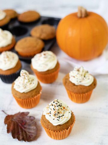 pumpkin spice cupcakes topped with cream cheese frosting and a whole pumpkin in the background.