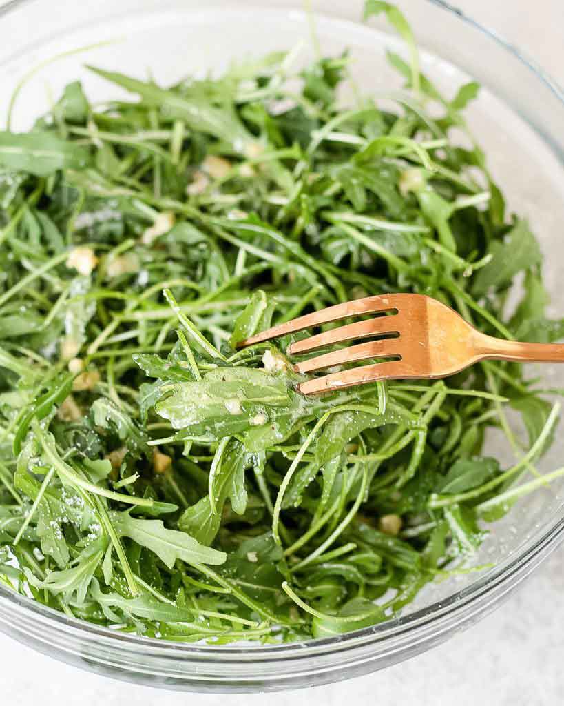 arugula salad in a serving bowl topped with simple dressing.