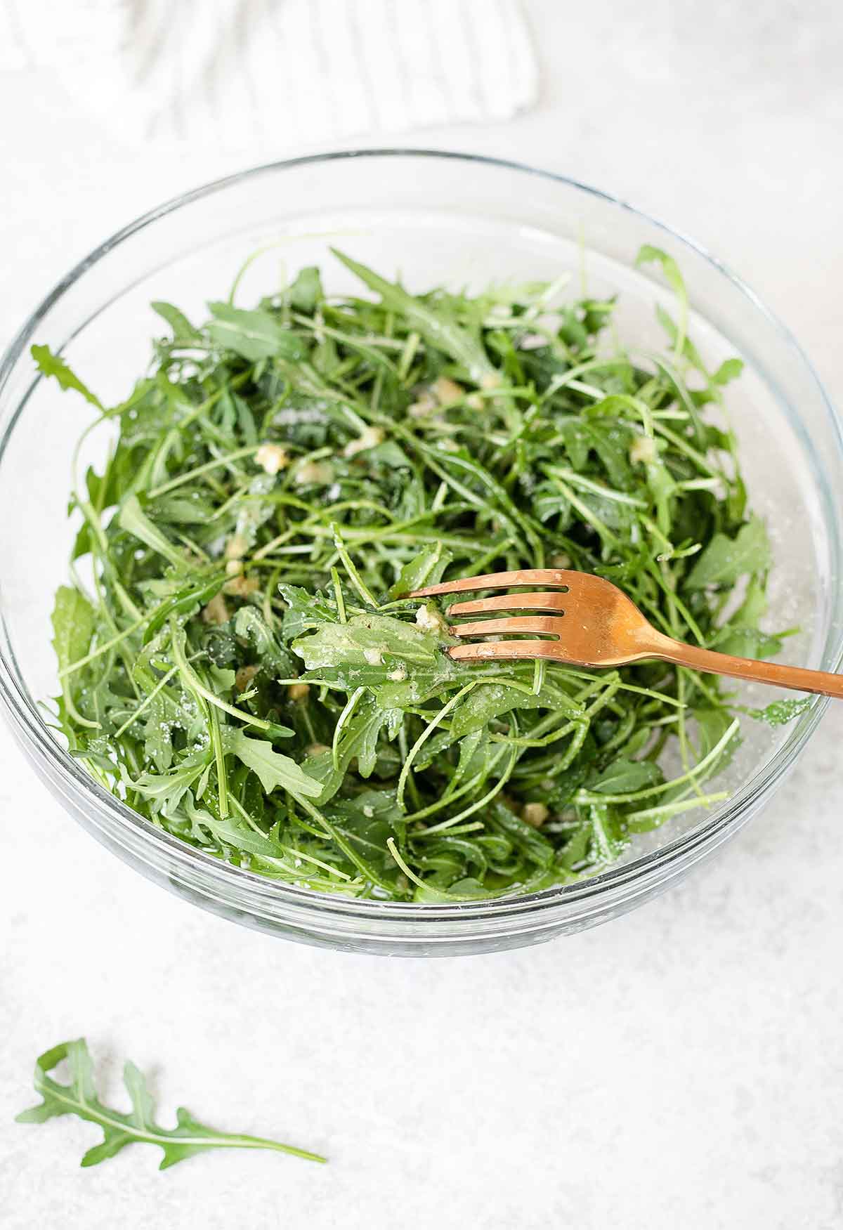 rocket salad in a serving bowl topped with garlic oil dressing.