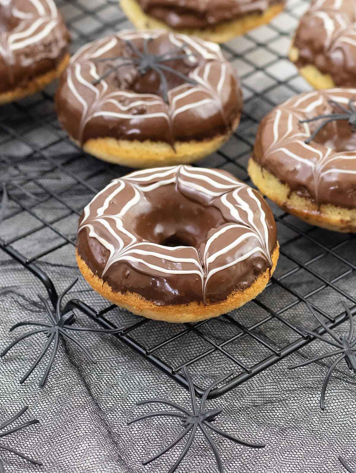 Halloween themed donuts decorated with web spider made from chocolate and some spiders around.