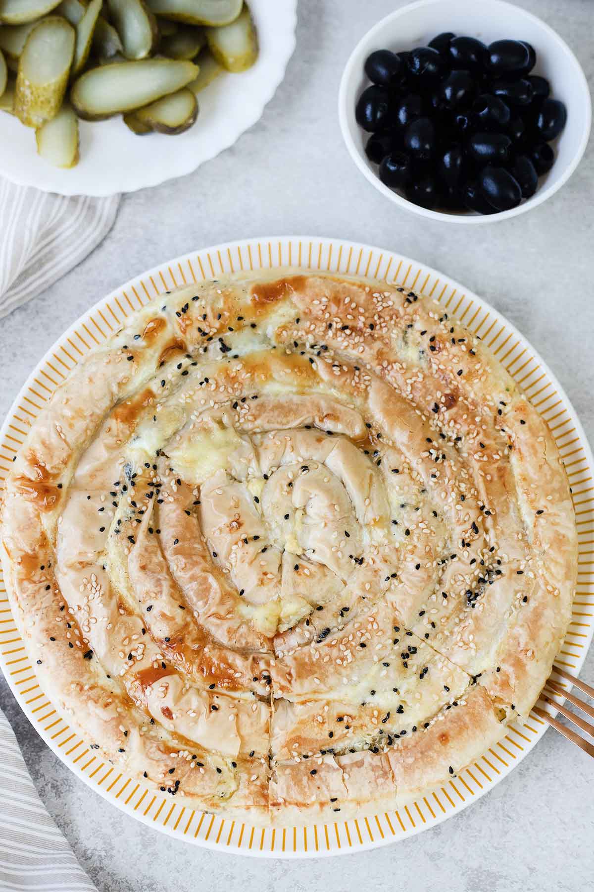 A whole Greek cheese pie (tiropita) in a serving plate topped with black seeds and sesame seeds.