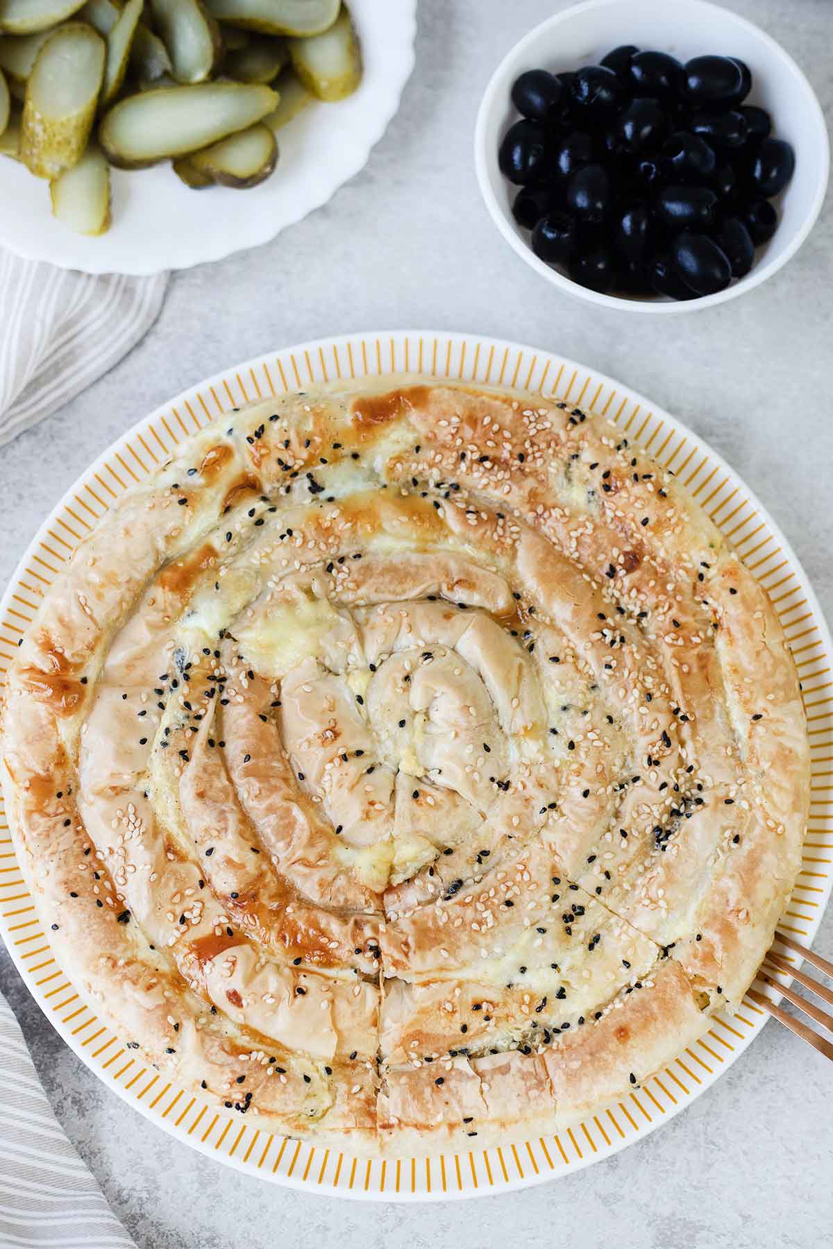 A whole Greek cheese pie (tiropita) in a serving plate topped with black seeds and sesame seeds.
