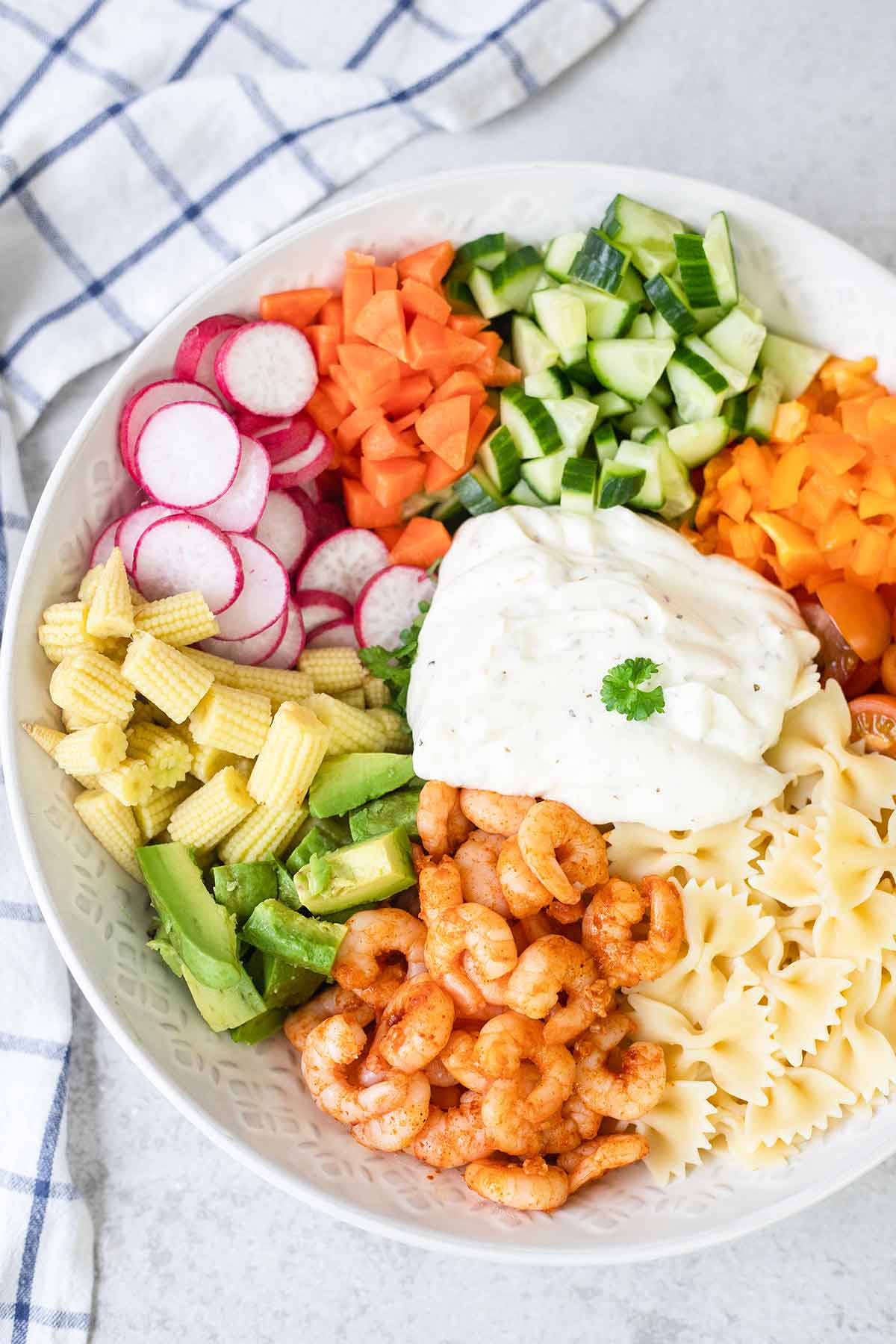 Adding the creamy dressing to the Italian shrimp pasta salad in the bowl.