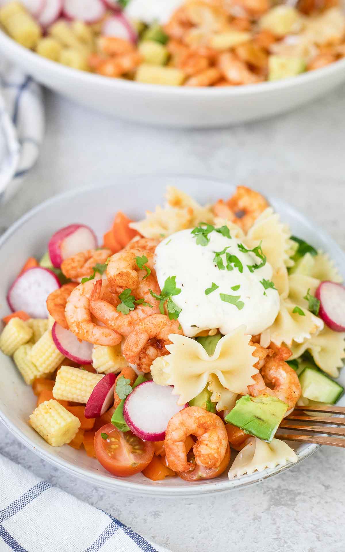 A bowl filled with Italian shrimp pasta salad and topped with a dollop of creamy dressing.
